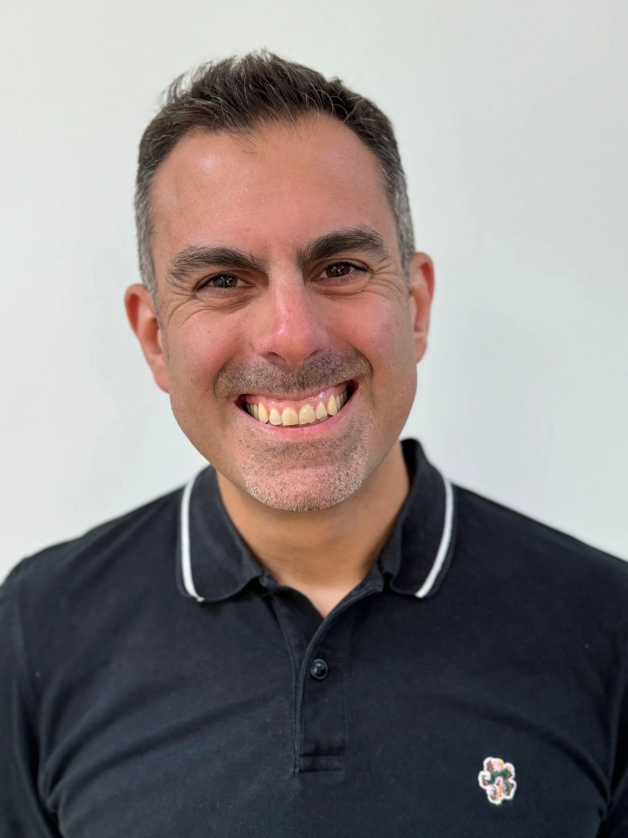 Seb Antoniou — storyboard artist, photographed in a black collared shirt against a white background.